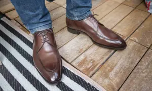 Ett par eleganta bruna läderskor med snörning, som sitter på en person med blå jeans. Skorna har en fin glans och ser ut att vara av hög kvalitet, trots att de har lite glappande skor-känsla.