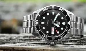 En närbild på en orient ray 2 dykarur med svart urtavla och silverfärgat armband, placerad på en träyta.