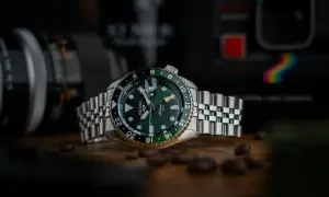 En grön Seiko GMT-klocka med en tvåfärgad bezel, omgiven av kaffebönor. Bakgrunden visar en kamera.