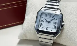 En stilren Cartier Santos-klocka i stål, ett exempel på exklusiva herrklockor, ligger på en kudde bredvid en vinröd klockbox.