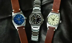 Tre Yema Wristmaster Traveller-klockor med blå, svart och krämfärgad urtavla, på en svart läderbakgrund.