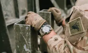 En soldat med moderna klockor på handleden, klädd i kamouflageuniform, håller i en metallkonstruktion.