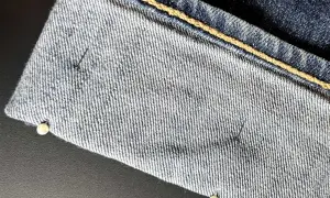 Närbild på jeans som ska vikas upp. Nålar håller tyget på plats.