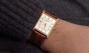 En elegant guldfärgad Seiko-klocka med brun läderrem på en arm. Dessa japanska klockor är kända för sin precision.