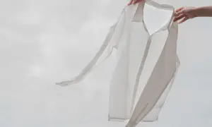 Två händer håller upp en vit, lätt skjorta i viskosmaterial mot en molnig himmel. Skjortan fladdrar i vinden.