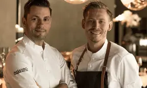 Två kockar ler mot kameran. Deras vita kockrockar och förkläden antyder en professionell miljö, kanske en restaurang som får bra allegrine recensioner.