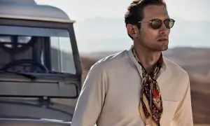 Man med solglasögon och en färgglad scarf, redo att knyta scarf för äventyr vid en gammal bil.