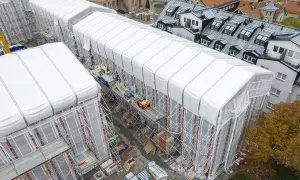 Byggarbetsplats i Sverige med vita presenningar över hus, ställningar och en gul kran. En pampuscher herr skulle uppskatta den ordning och reda som råder.