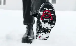 En person går i snön med svarta stövlar. Sulorna har ett mönster och röda detaljer för att undvika hala skor.