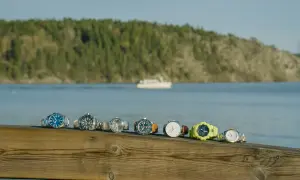 En rad olika klockor, från eleganta till sportiga, ligger uppradade på en träbrygga med en båt i bakgrunden. Varje boett klocka berättar sin egen historia.