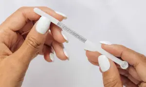 Händer med vita naglar mäter fingerstorlek med ett mätverktyg som visar ring storlek 15.