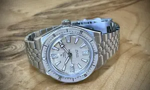 En Yema Superman dykarklocka med silverfärgad urtavla och ett unikt, bikakeformat metallarmband ligger på ett träbord.