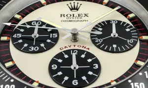 En närbild av en Rolex Daytona, en ikonisk klocka som Paul Newman själv bar. Den har tre svarta urtavlor på en krämfärgad bakgrund.