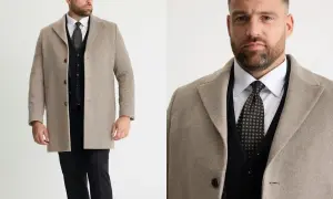 Man i beige jacka till kostym, med svart väst och mönstrad slips.
