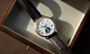 Ett elegant armbandsur med brunt läderband och ett synligt mekaniskt urverk. Klockan ligger i en träask.
