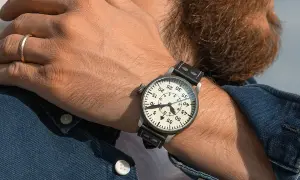 En man med skägg bär en klassisk fliegerklocka med tydlig urtavla och läderarmband.