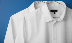 Två vita skjortor hänger på galgar mot en blå bakgrund. De ser ut som om de precis kommit från en **dry cleaner**, perfekt strukna och redo att bäras.
