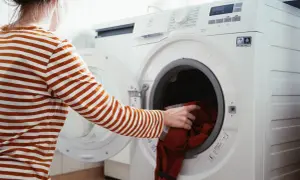 Person lägger röd tröja i tvättmaskin, redo för tvätt och gore tex impregnering.