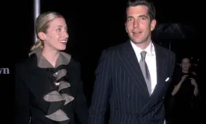 Carolyn Bessette Kennedy och John F. Kennedy Jr. på en tillställning. Hon bär en svart kavaj med volanger, han en randig kostym.