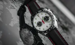 Kronograf med vit urtavla och svarta subdials, ett mecaquartz-ur med läderband, reflekteras i en våt yta.