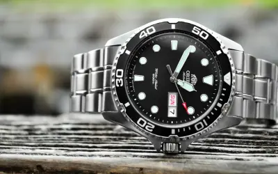 En närbild på en orient ray 2 dykarur med svart urtavla och silverfärgat armband, placerad på en träyta.