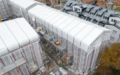 Byggarbetsplats i Sverige med vita presenningar över hus, ställningar och en gul kran. En pampuscher herr skulle uppskatta den ordning och reda som råder.
