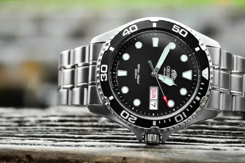 En närbild på en orient ray 2 dykarur med svart urtavla och silverfärgat armband, placerad på en träyta.