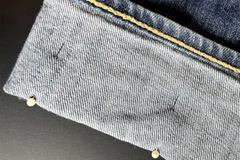 Närbild på jeans som ska vikas upp. Nålar håller tyget på plats.