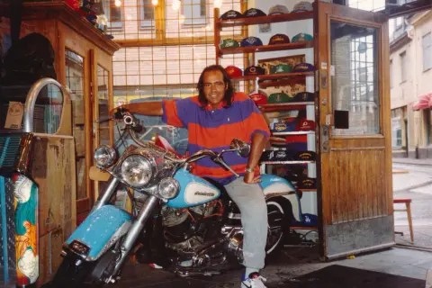 Man på motorcykel i en butik med kepsar, kanske en del av "Broadway & Sons" sortiment.