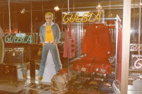 Reklam för GULBLA med en man i jeans, gul t-shirt och blå jacka. Röd jacka och byxor visas också.