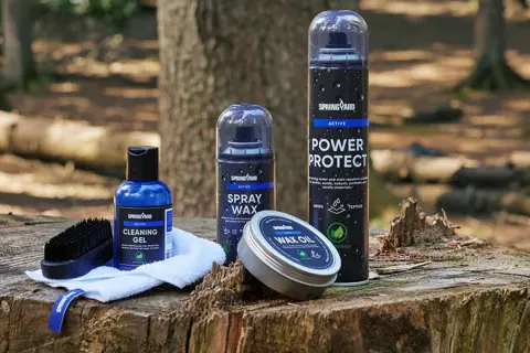 Produkter för impregnering av syntetskor: rengöringsgel, sprayvax, power protect och wax oil, placerade på en trädstubbe i skogen.