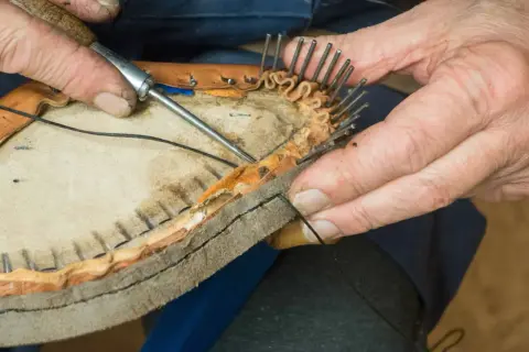 Händer syr ihop en lädersko med nål och tråd. Detaljerad bild av skotillverkning.