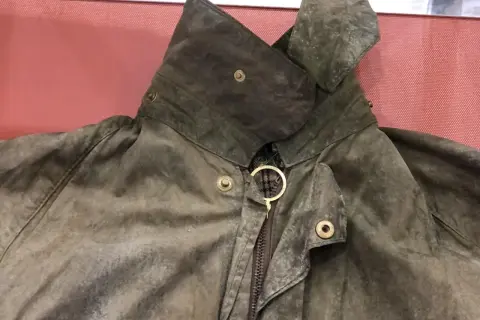Detaljerad bild av en sliten Barbour-jacka, redo att laga. Kragen är uppfälld och visar dragkedjan med en gyllene ring.