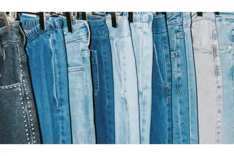 En rad blå jeans hänger på galgar, redo att stryka. Olika nyanser av denim, från mörkblått till ljusblått, skapar en visuell fest.