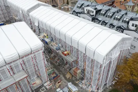 Byggarbetsplats i Sverige med vita presenningar över hus, ställningar och en gul kran. En pampuscher herr skulle uppskatta den ordning och reda som råder.