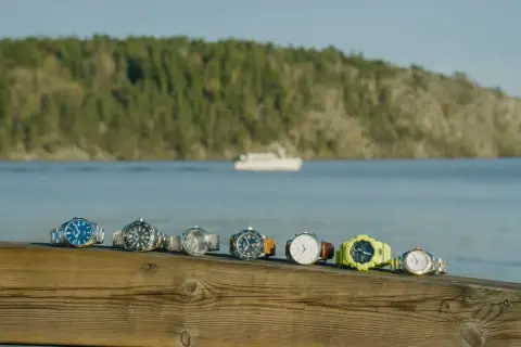 En rad olika klockor, från eleganta till sportiga, ligger uppradade på en träbrygga med en båt i bakgrunden. Varje boett klocka berättar sin egen historia.