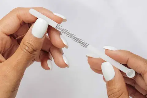 Händer med vita naglar mäter fingerstorlek med ett mätverktyg som visar ring storlek 15.