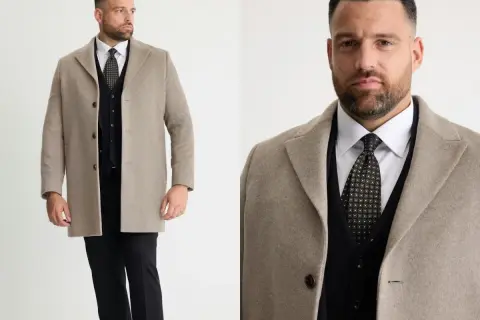 Man i beige jacka till kostym, med svart väst och mönstrad slips.