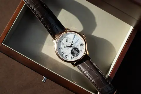 Ett elegant armbandsur med brunt läderband och ett synligt mekaniskt urverk. Klockan ligger i en träask.