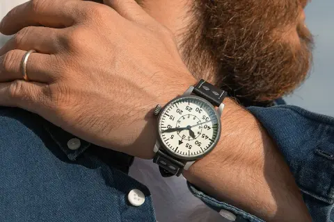 En man med skägg bär en klassisk fliegerklocka med tydlig urtavla och läderarmband.