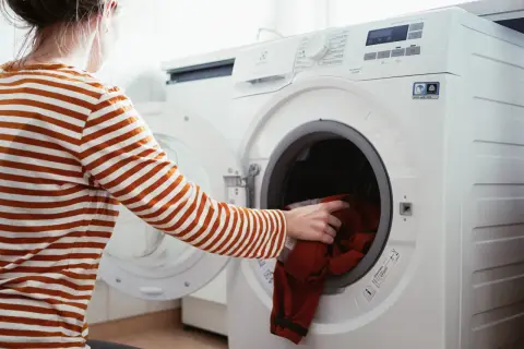 Person lägger röd tröja i tvättmaskin, redo för tvätt och gore tex impregnering.
