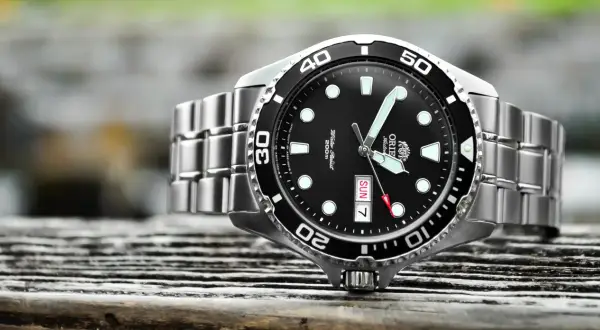 En närbild på en orient ray 2 dykarur med svart urtavla och silverfärgat armband, placerad på en träyta.