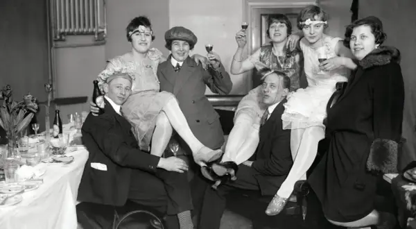 Festligt sällskap i mode 1920-tal, med kvinnor i klänningar och män i kostym, skålar och njuter av festen.