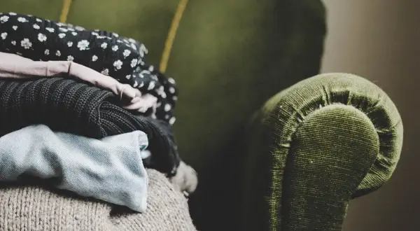 En hög med kläder ligger på en grön soffa. Kanske dags för lite dry clean hemma?