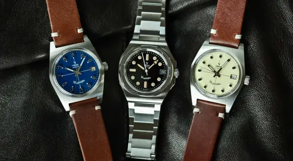 Tre Yema Wristmaster Traveller-klockor med blå, svart och krämfärgad urtavla, på en svart läderbakgrund.