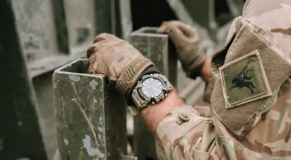 En soldat med moderna klockor på handleden, klädd i kamouflageuniform, håller i en metallkonstruktion.