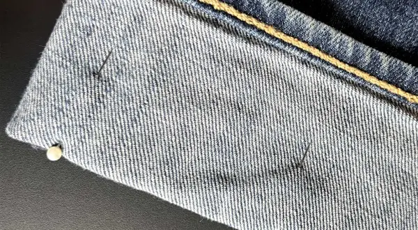 Närbild på jeans som ska vikas upp. Nålar håller tyget på plats.