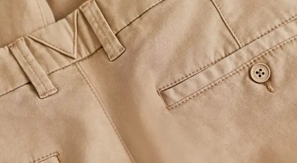 Detaljbild på beige chinos med snygga sömmar och en knapp. Perfekt bas för många olika skor till chinos.