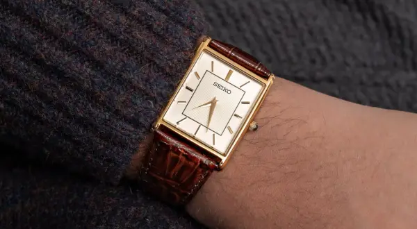 En elegant guldfärgad Seiko-klocka med brun läderrem på en arm. Dessa japanska klockor är kända för sin precision.