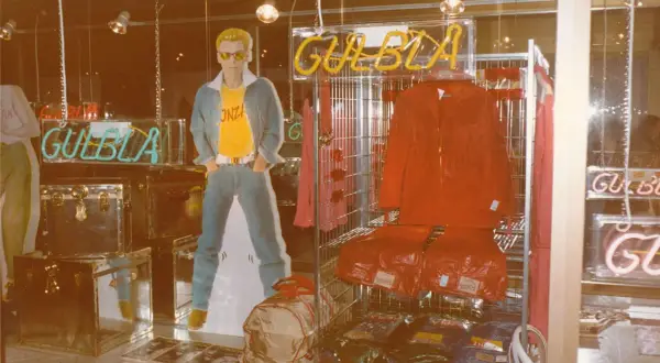 Reklam för GULBLA med en man i jeans, gul t-shirt och blå jacka. Röd jacka och byxor visas också.